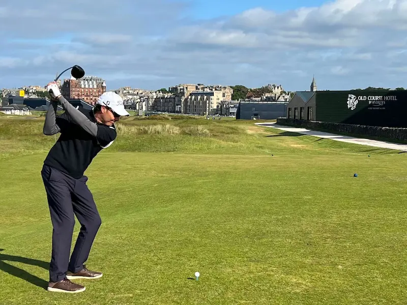Golfer preparing a controlled tee shot on a historic links-style course under clear skies