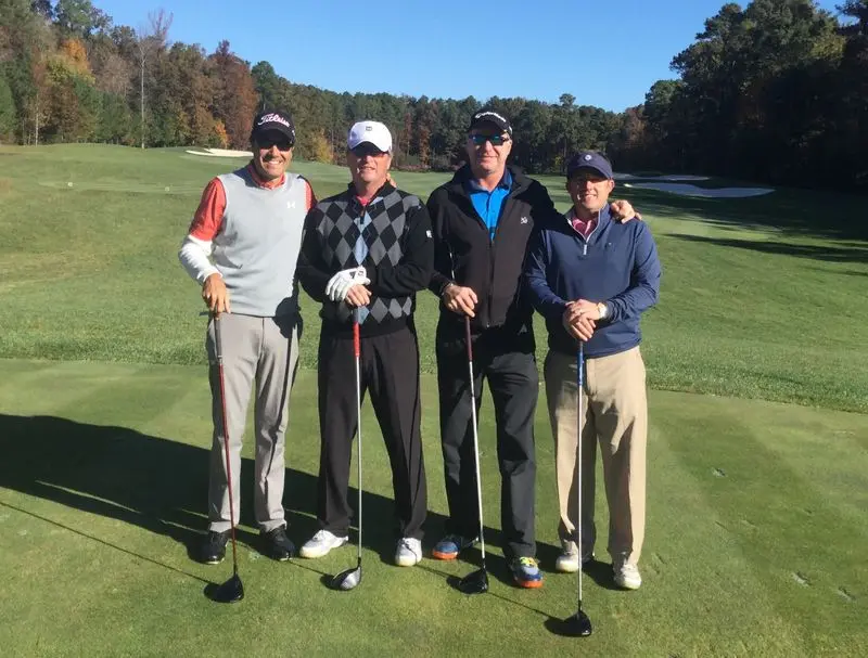 Four golfers standing together on a fairway holding clubs, captured during a relaxed round on a well-maintained course with trees in the background