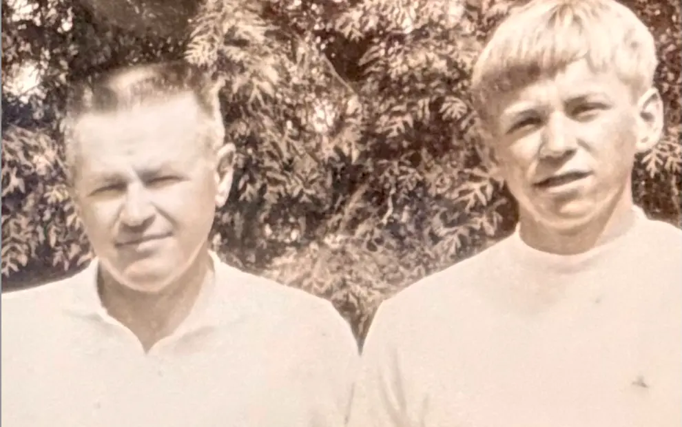 Vintage black and white photograph showing two young men standing outdoors with trees in the background
