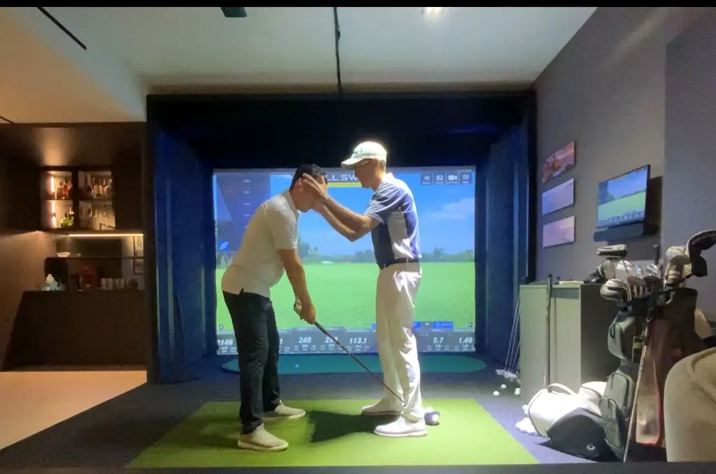 Golf instructor adjusting a student’s posture during an indoor lesson using a swing simulator, focused on improving setup and body alignment