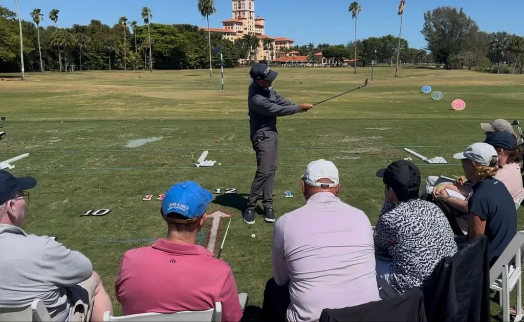 Golf instructor demonstrating swing technique during an indoor lesson while students observe, using visual feedback and training tools in a controlled learning environment