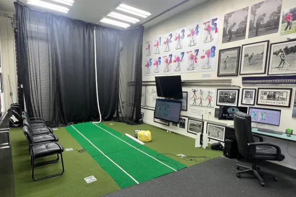 Indoor golf training studio featuring swing analysis mats, video screens, seating area, and instructional displays for focused practice