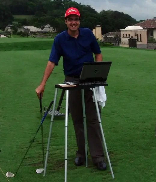 Instructor using a laptop on the practice area to review swing analysis with clubs positioned nearby