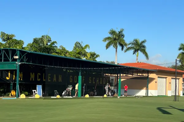 Golfers practicing at an outdoor training area with covered hitting bays and well-maintained turf at Jim McLean Golf School
